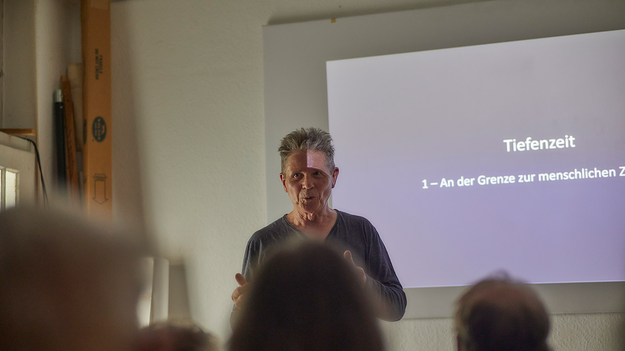 Ein Mann, der eine Rede hält. Im Vordergrund unscharf und von hinten die Köpfe einiger Zuschauer.